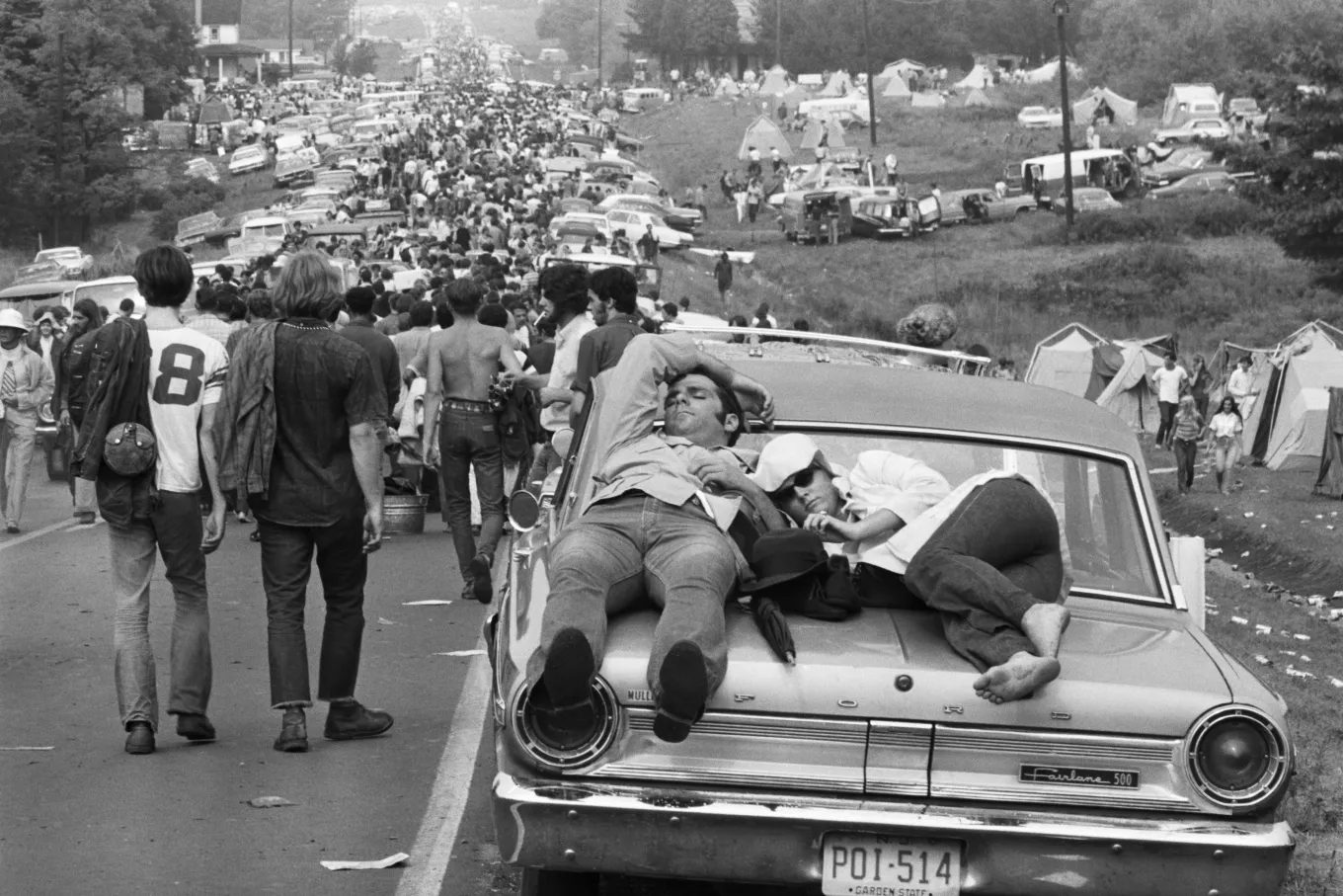 A couple sleeping on a car hood amid the endless traffic and crowds heading to Woodstock, 1969
